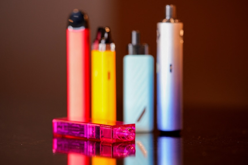 five colourful vapes standing on a black-coloured counter