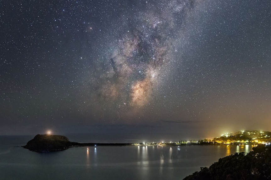 a galaxy above a dark strip of land over the sea