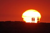 Two people silhouetted by a blazing yellow sun against a firey red backdrop.