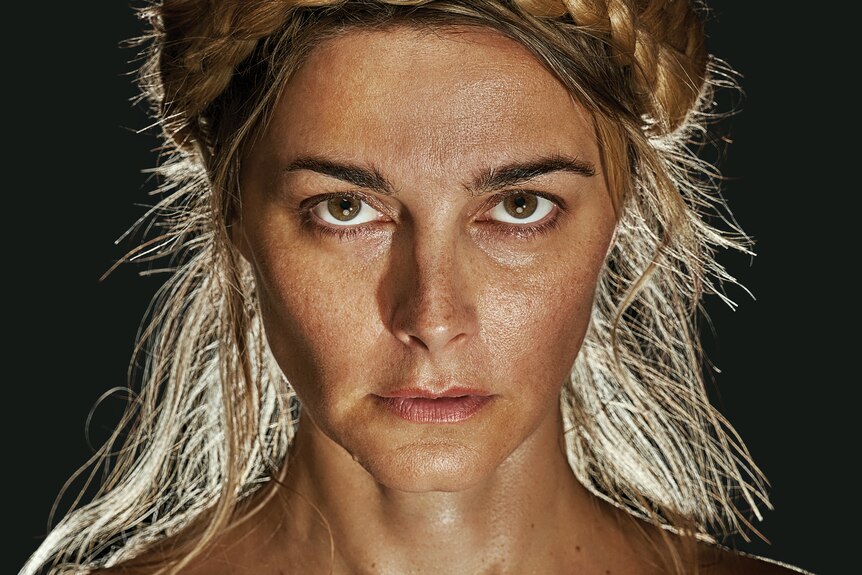 A close up of a woman in her early 40s, black background, lit from behind, staring determinedly