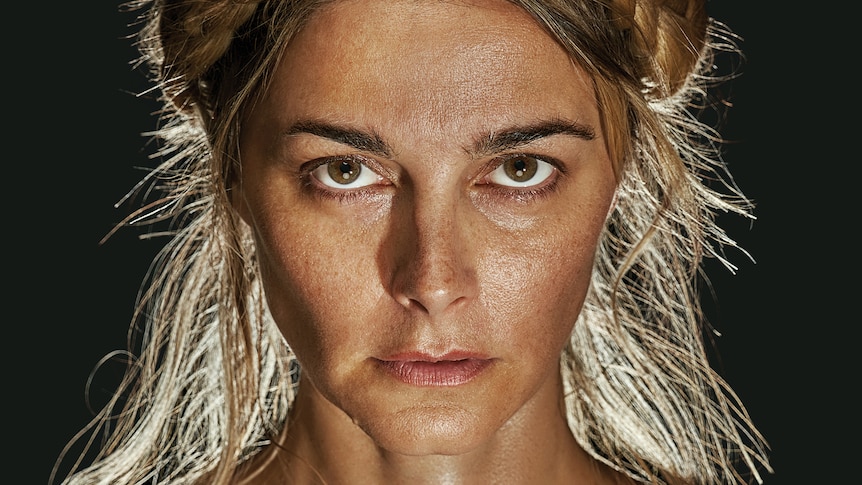 A close up of a woman in her early 40s, black background, lit from behind, staring determinedly