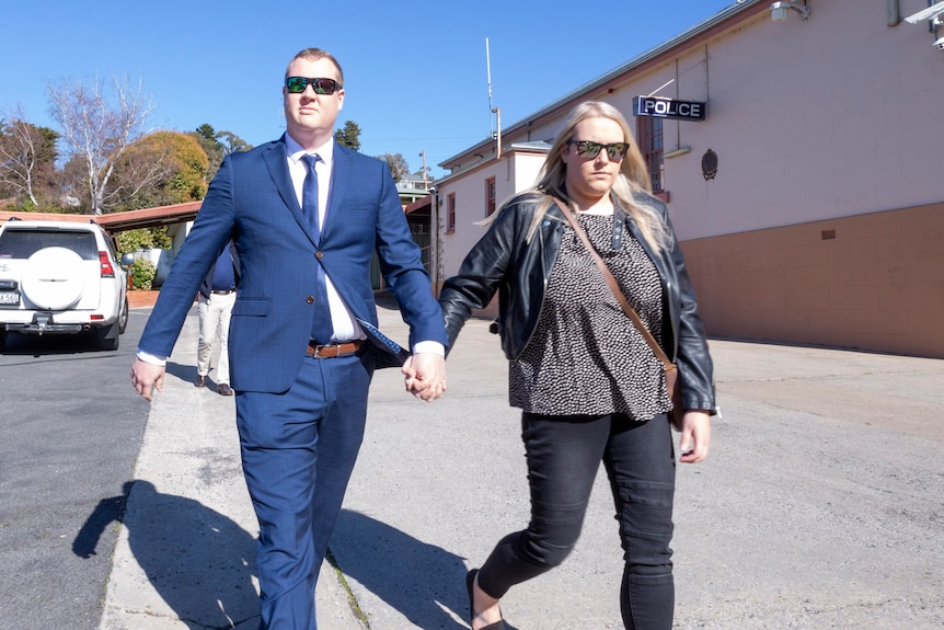 a man wearing glasses and a blue suit holds hands with a woman