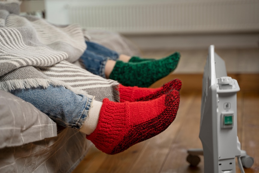 A heater on the floor with two feet warming up next to it. The feet have socks on