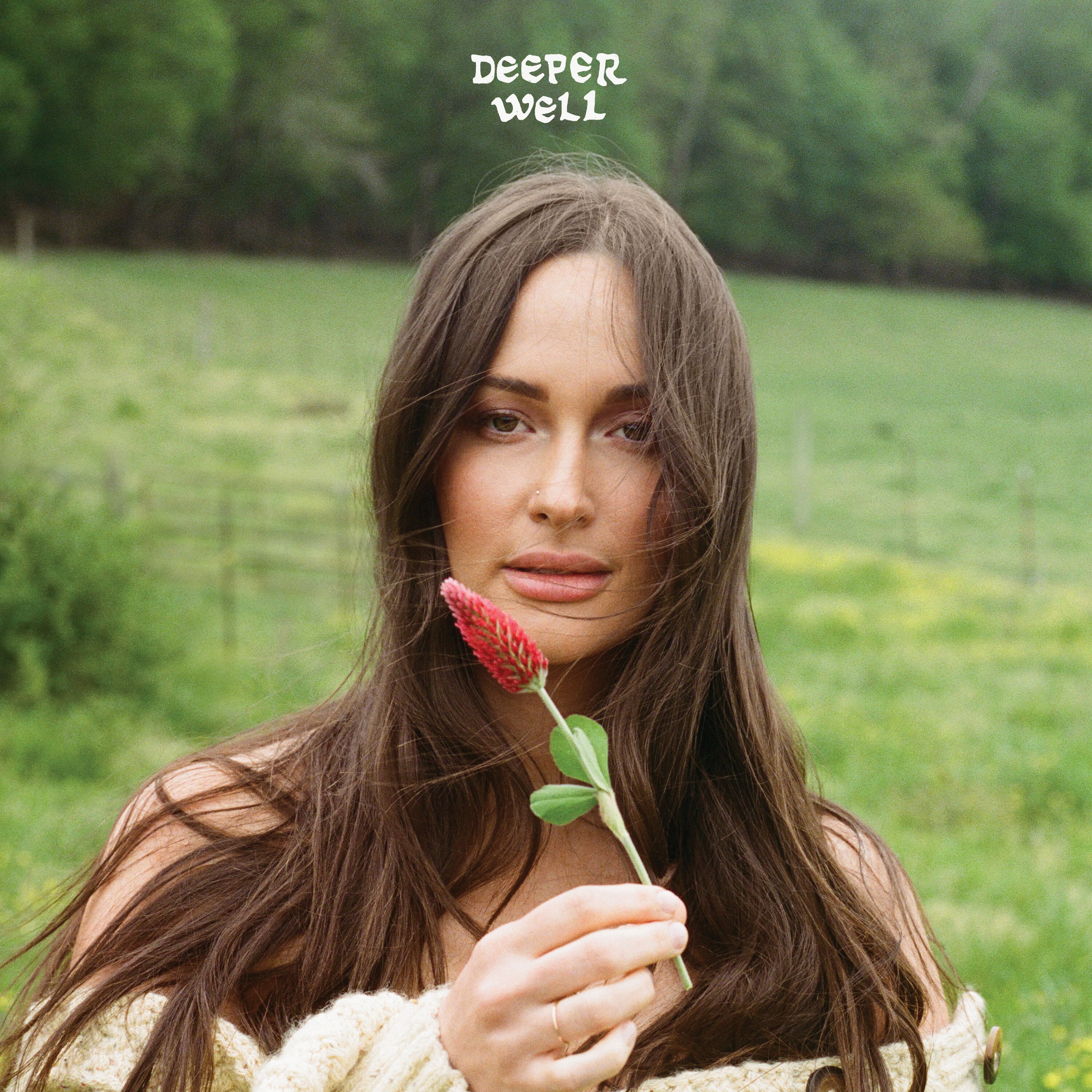 Brunette woman offers up a crimson clover as she stands in a green field with text: DEEPER WELL