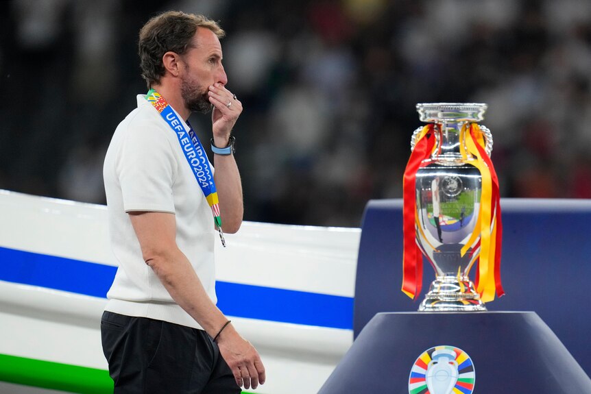 Gareth Southgate walks past a trophy and holds his mouth