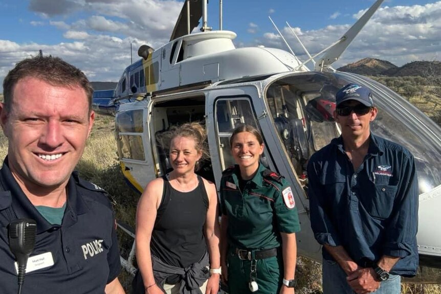 A woman stands with three people in front of a helicopter - two are in police and paramedic uniforms. 