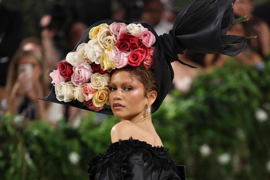 Zendaya looks over her shoulder, a bouquet of flowers in her hair.