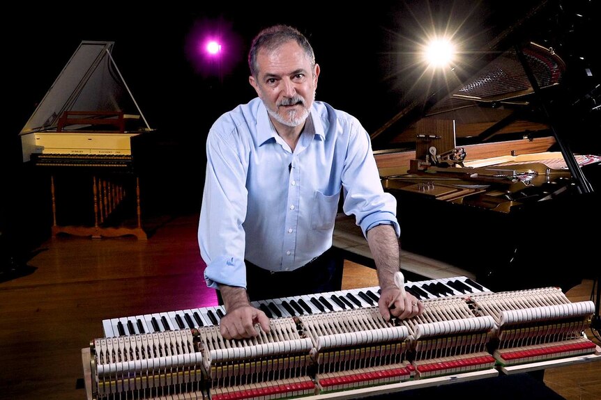 Ara Vartoukian with his sleeves rolled up leaning on the keyboard mechanism of a grand piano.