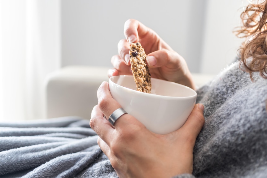 Close-up of woman eating a chocolate chip cookie over a cup of tea.