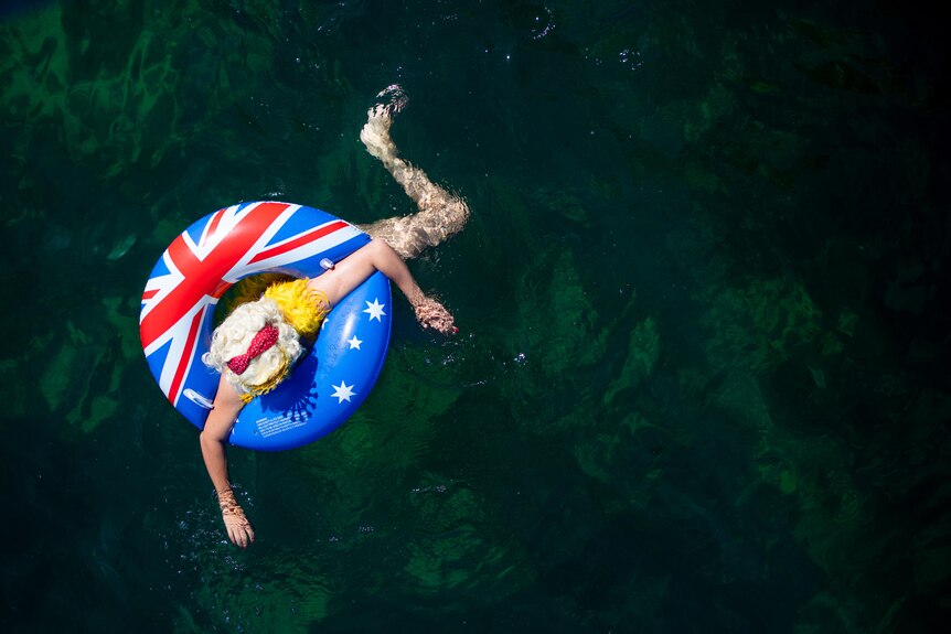 A birdsye perspective of a swimmer with blue floatie and blonde wig swimming in the ocean.