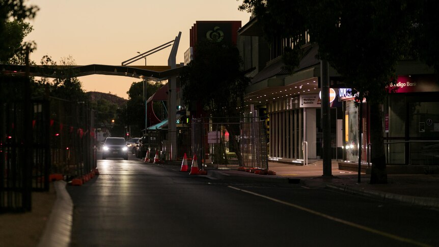 A car with its headlights on drives down a quiet street around dusk