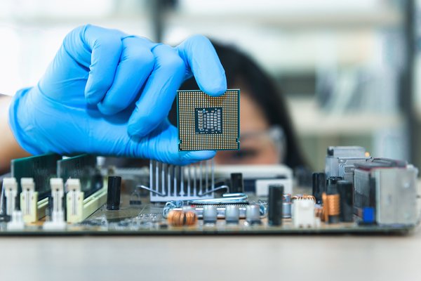 A gloved woman holding up a chip above electronics.