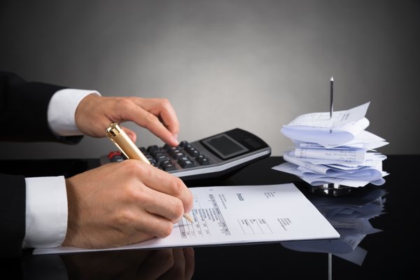 Hand is writing on a sheet of paper with a calculator.