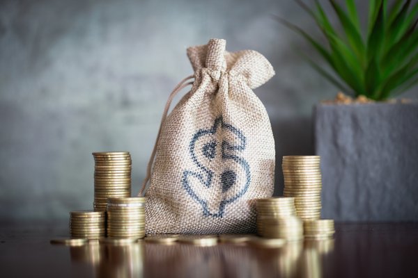 Stacks of coins next to a burlap bag with dollar sign.