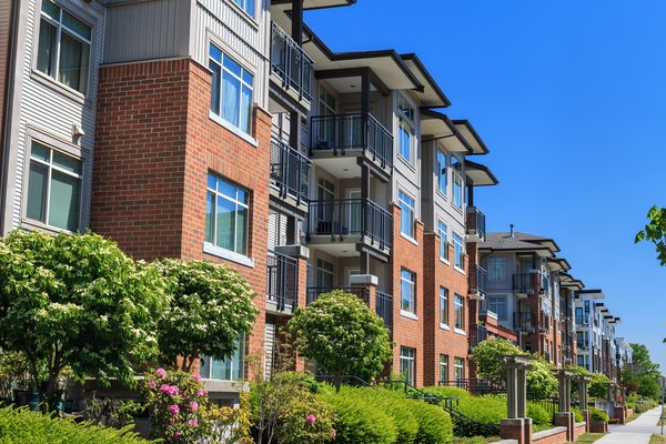 Apartment buildings with trees and flowers along a city sidewalk.