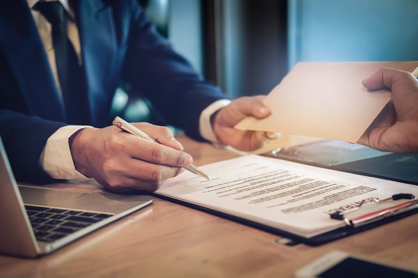 Person signing a contract while handing an envelope to another person.