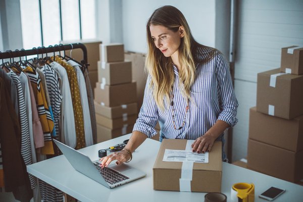 Person using laptop and preparing small box for shipping.