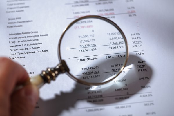 A hand holding a magnifying glass up to some financial paperwork.