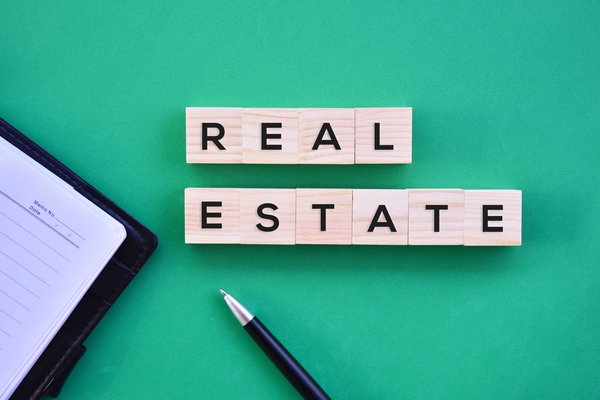 A pen and memo book lying next to blocks that spell out real estate.