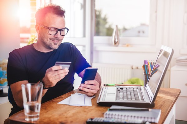 A person is holding a credit card and smartphone while sitting in front of a laptop.