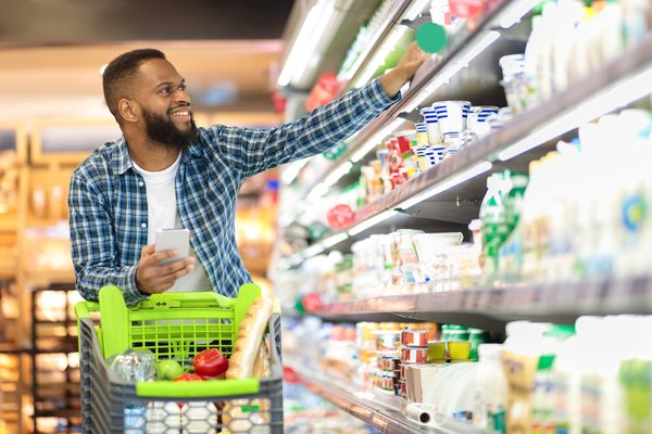 Smiling person pushing a shopping cart in a grocery store..