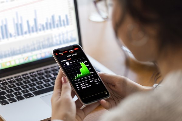 A person looking at stock charts on a computer and phone.