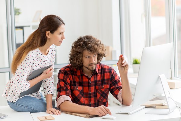 Person pointing to a computer screen while another person looks on.