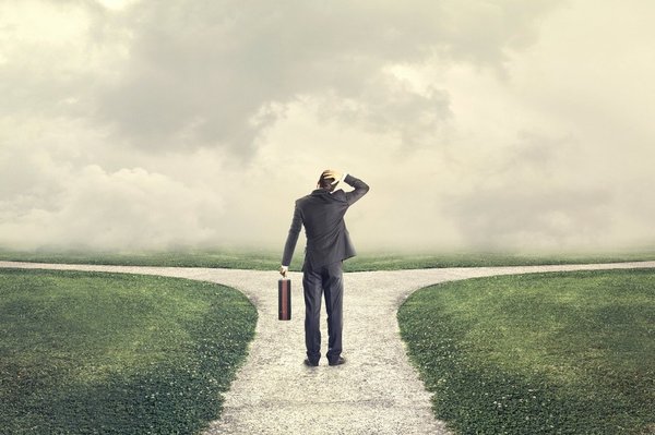 Business man has his hand on his head while looking at a fork in the road.