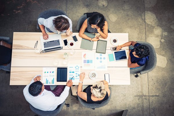 Aerial view of five people sitting around table and discussing charts in an office.