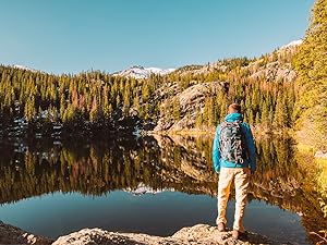 Photo shows person standing, admiring a mountain lake.