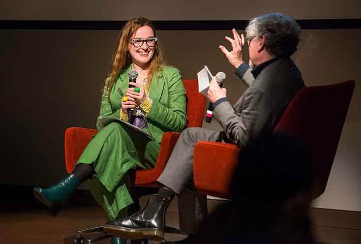 woman and man sitting in chairs on stage in conversation