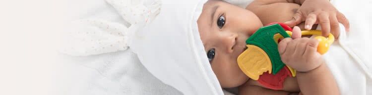 Baby wrapped in a bath towel and holding teething toy while laying down.