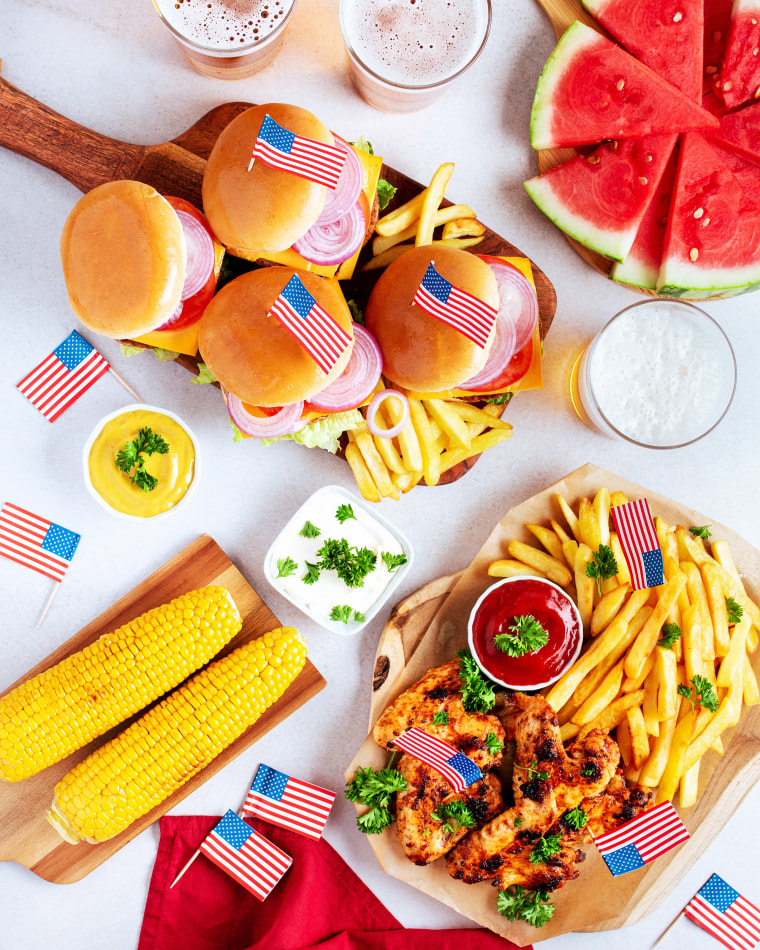 4th of July table decorations with burgers, chicken wings, corn, fries and beer, decorated with american flags, top view