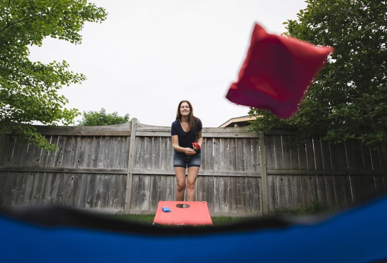 Woman throwing a bean bag in a corn hole game shot from below.