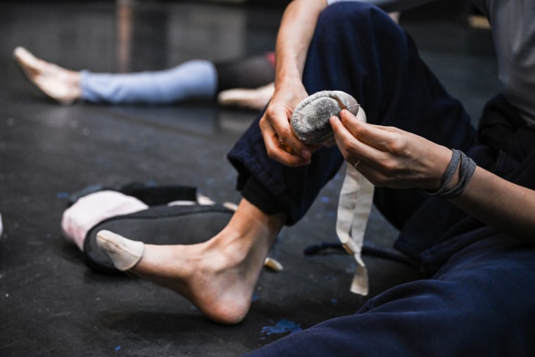 A hand holds a scuffed up pointe shoe, preparing to place it on their foot