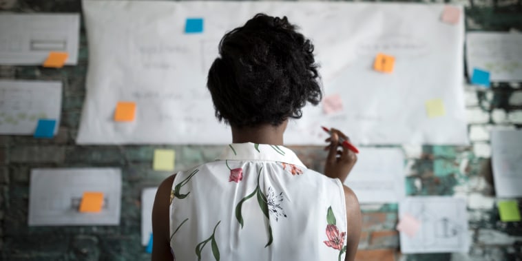 Creative businesswoman brainstorming, reviewing flow chart hanging on brick wall in office