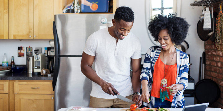 Happy man cutting tomatoes while standing with girlfriend at home