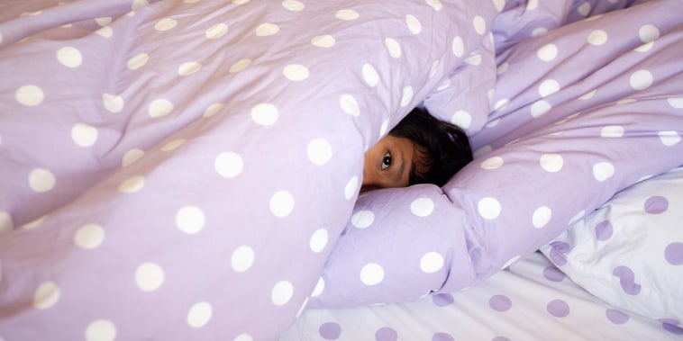 A little girl hides under the covers