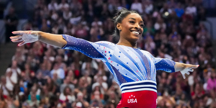 Simone Biles smiles with her arms extended by her sides