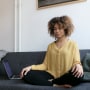 Image: Young woman sitting on couch at home next to laptop meditating