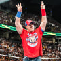 John Cena stands in the wrestling ring raising both arms and doing the "okay" hand symbol