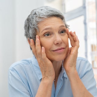 Beautiful senior woman checking her face skin and looking for blemishes. Portrait of mature woman massaging her face...