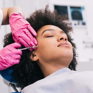 Attractive young African woman is getting a rejuvenating facial injections. She is sitting calmly at clinic. The expert...