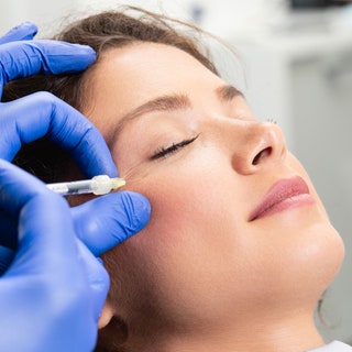 Woman getting Botox injections into her crow's feet near eye area on right side of face
