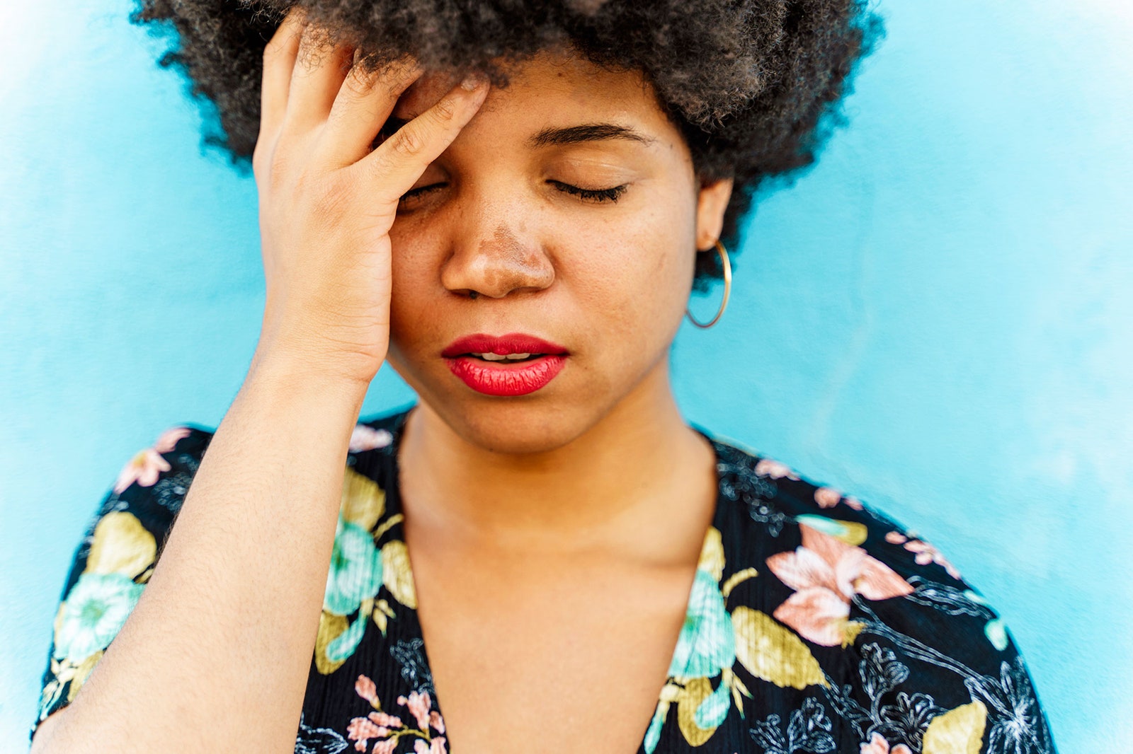 woman touching her forehead with eyes closed in front of blue background