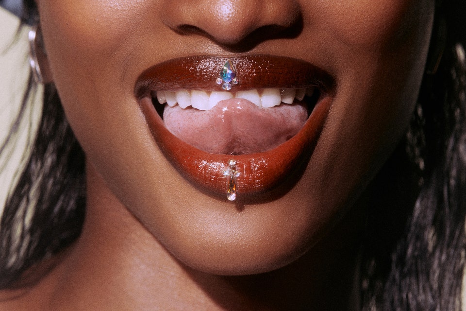 close-up image of woman wearing red-brown lipstick, opening mouth with her tongue on her teeth