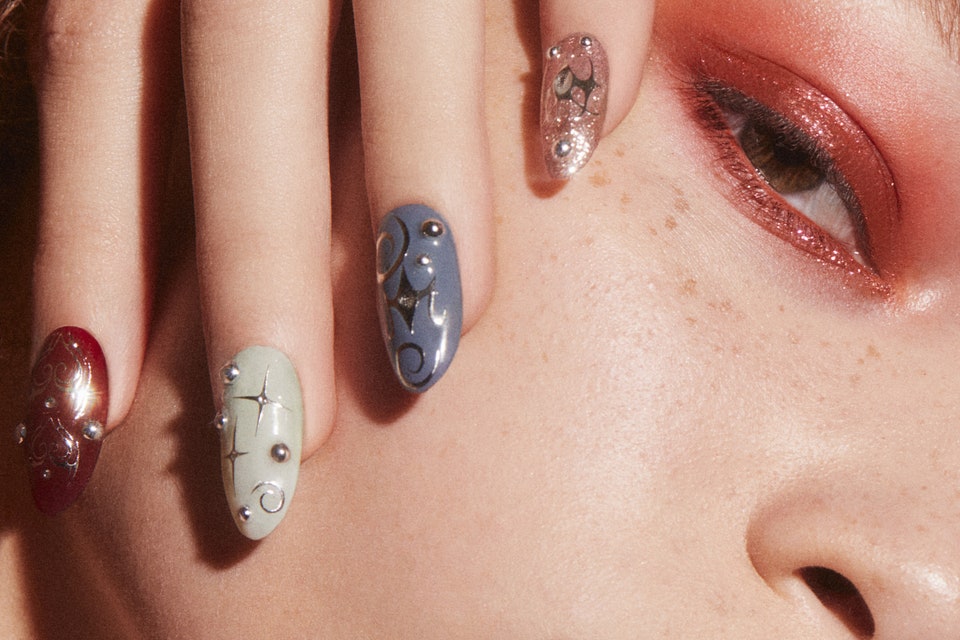 closeup image of woman holding hand with long colorful nails on cheek