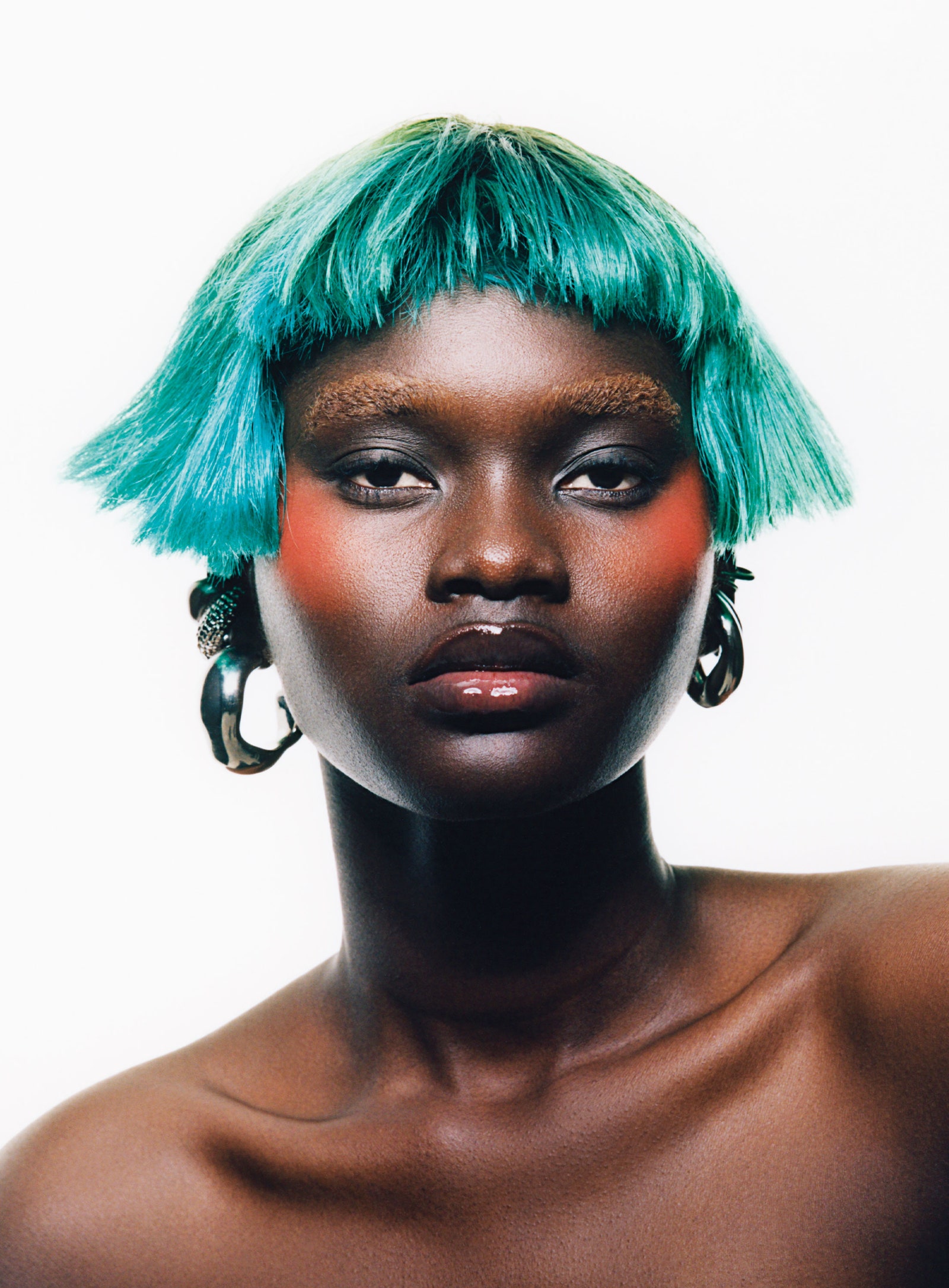 Close shot of model wearing a teal short bob while wearing orange blush.