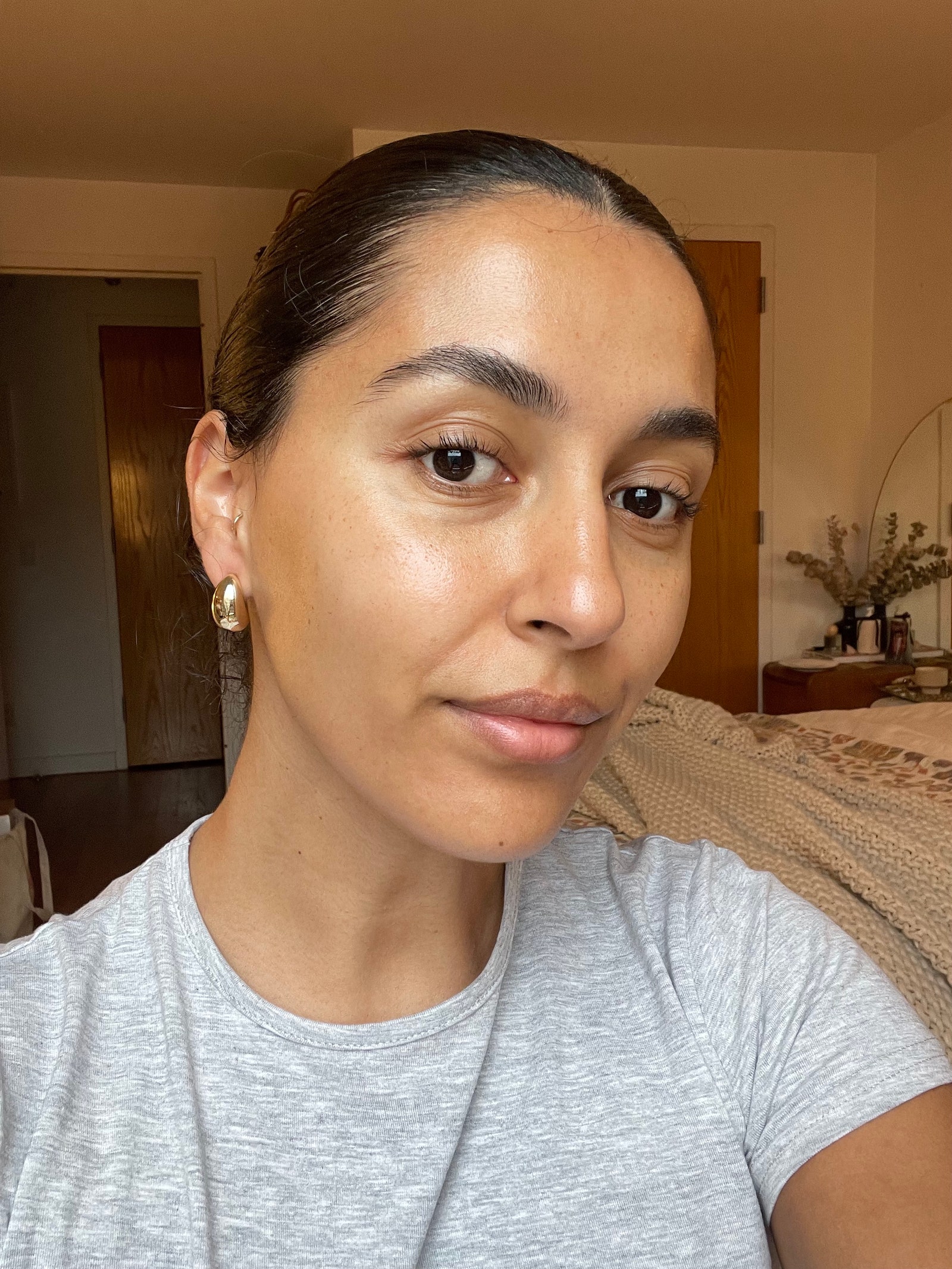 A woman with a slicked back bun smiling at camera wearing a gray tshirt