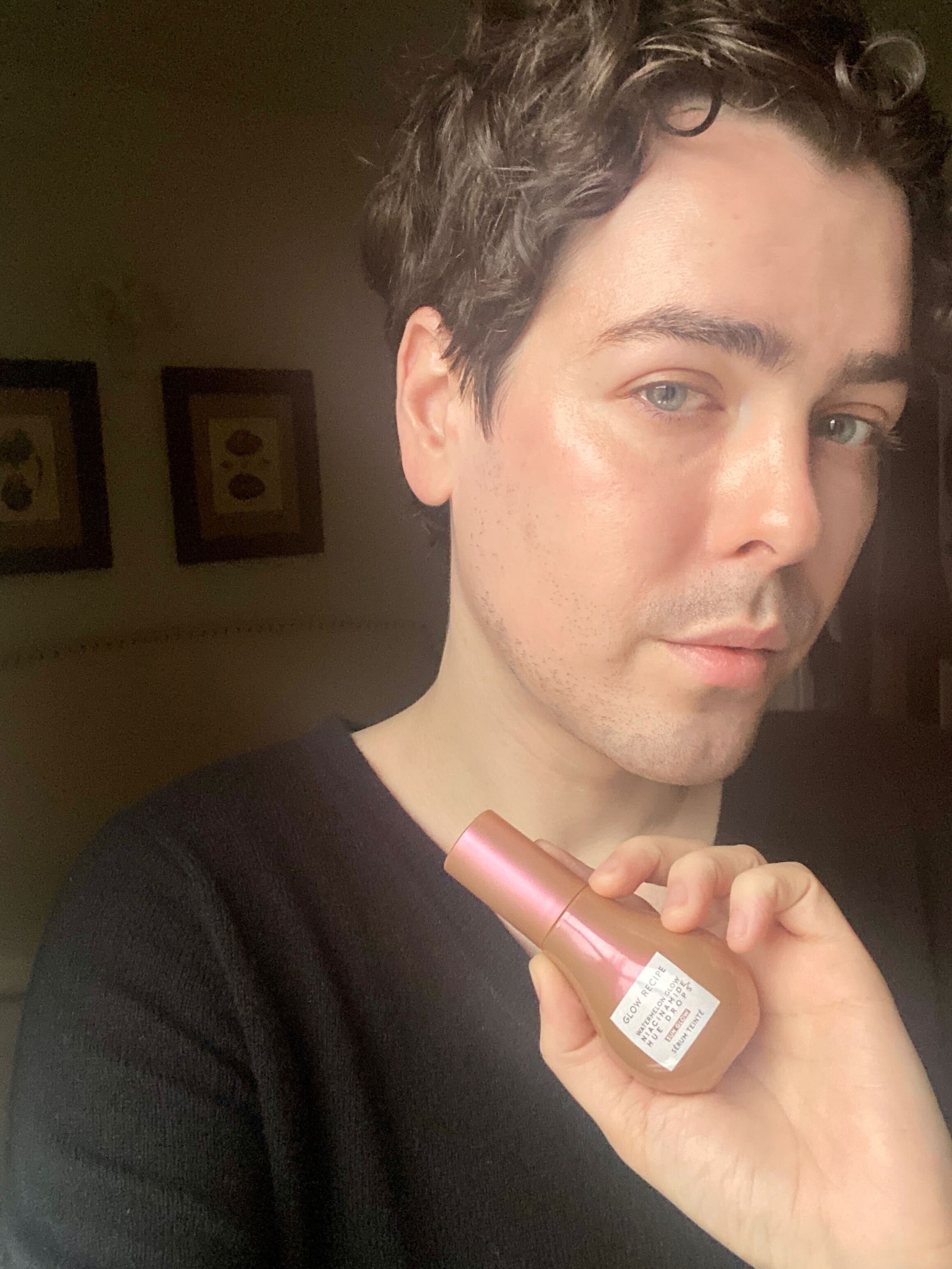 Allure editor taking a selfie holding a bottle of a bronzed serum wearing a black tshirt